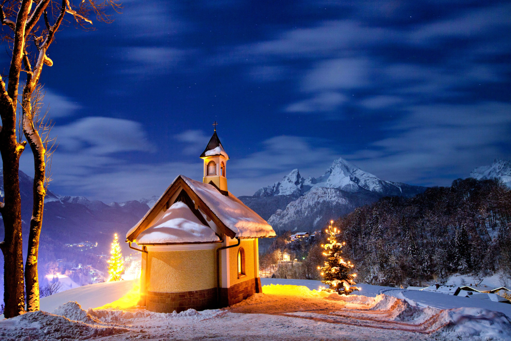 Schneebedeckte Kapelle bei Nacht, umgeben von winterlicher Landschaft und Bergen.