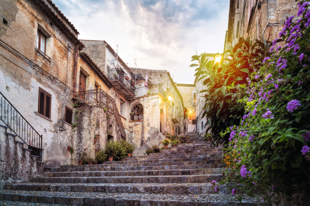 Hübsche Gasse mit Blumen und historischen Gebäuden in einem italienischen Dorf bei Sonnenuntergang.
