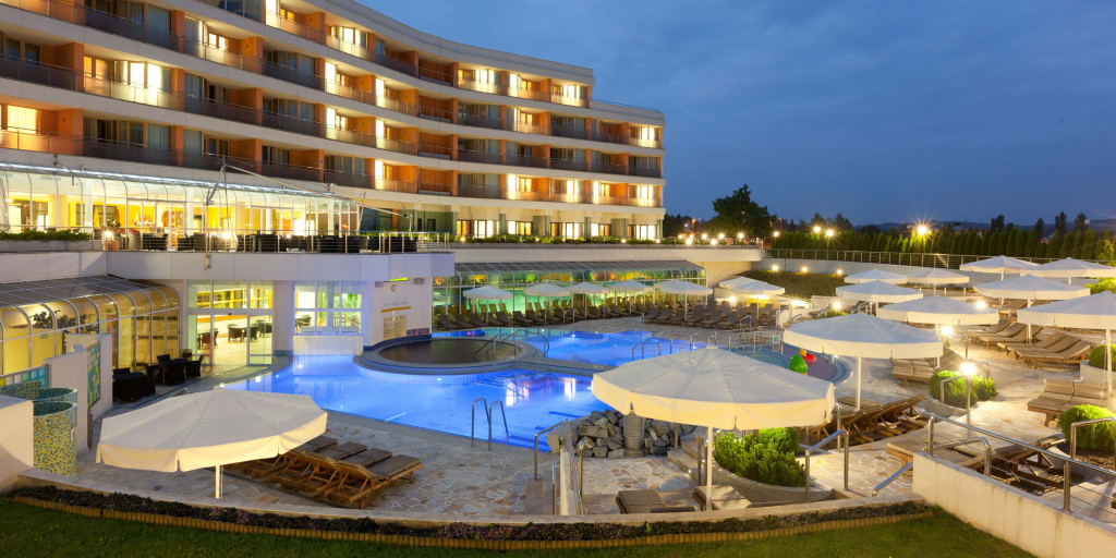 Therme 3000 mit Pool und Liegen vor einem modernen Gebäude bei Dämmerungslicht.